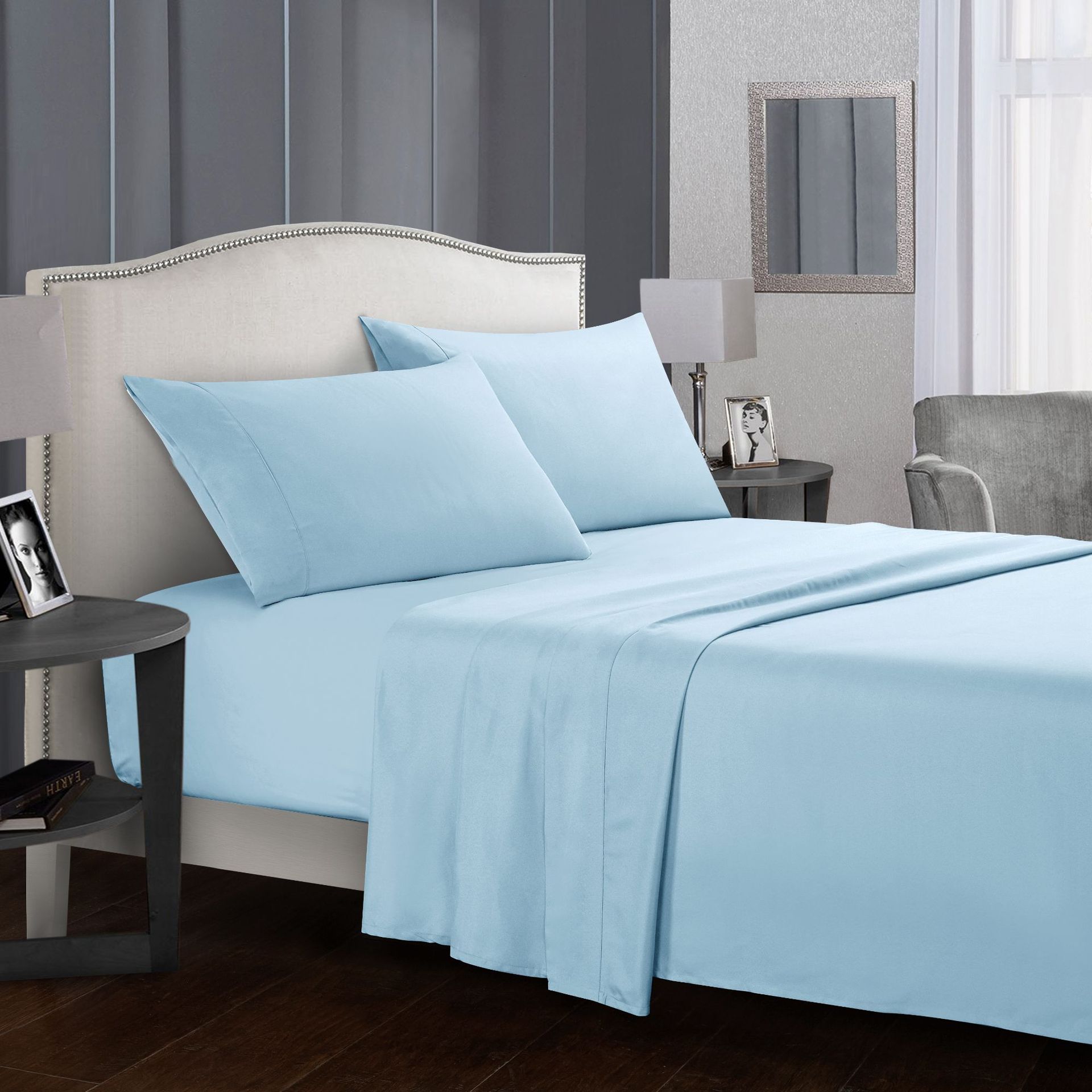Blue bedding set on a bed in a bedroom with gray walls and furniture.