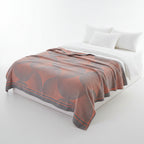 Patterned throw blanket on a bed with pillows and a window in the background