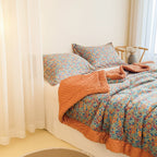 Floral bedding set with orange throw on a bed in a bedroom.