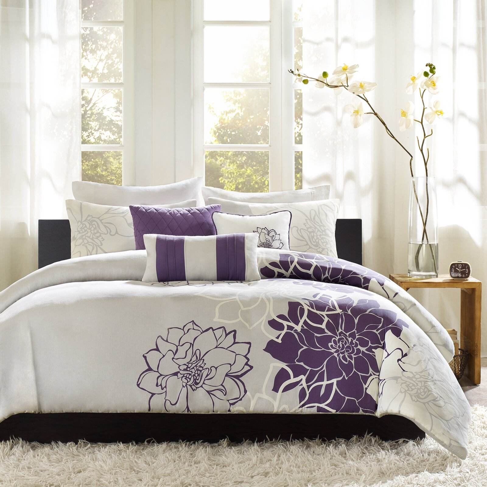 Bedroom with white bedding and purple floral patterns, featuring a bed and side table.