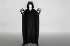 A black cat-themed hooded blanket/cape wear garment displayed on a white mannequin against a light gray studio background. The hood has pink inner ears and yellow eyes, and the glove-like hands have pink paw pads.