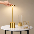 Gold dimmable table lamp on a marble surface with a hand pressing the top to adjust brightness.