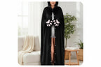 A woman wearing a long black hooded blanket cape with white embroidered face details and white paw-print accents on the sleeves, standing in a bright living room. Text below reads 'Convertible Blanket To Stylisih Cape' and 'Premium Stitching With Embroidered Face'.