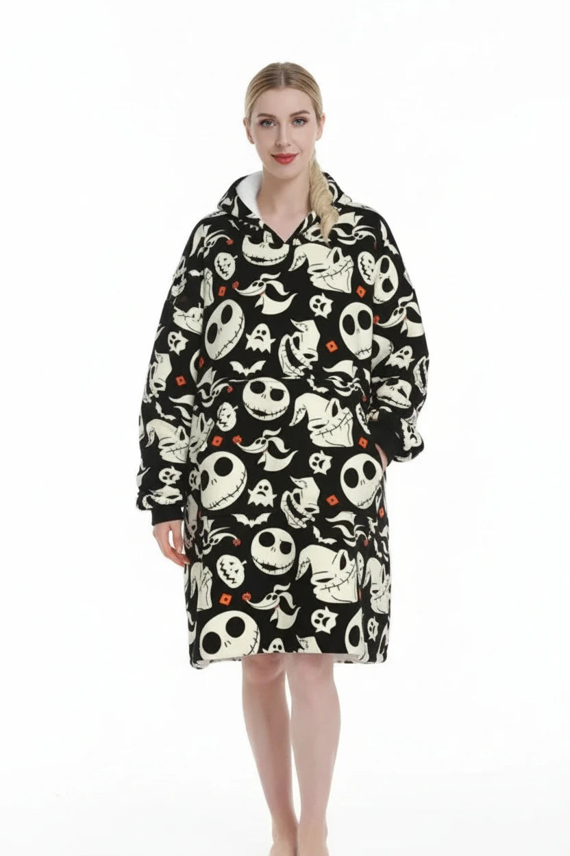 A person wearing a hooded blanket poncho with an all-over Halloween-themed print featuring Jack Skellington skulls, ghosts, bats, and small orange diamond accents on a black background, against a plain white studio backdrop.
