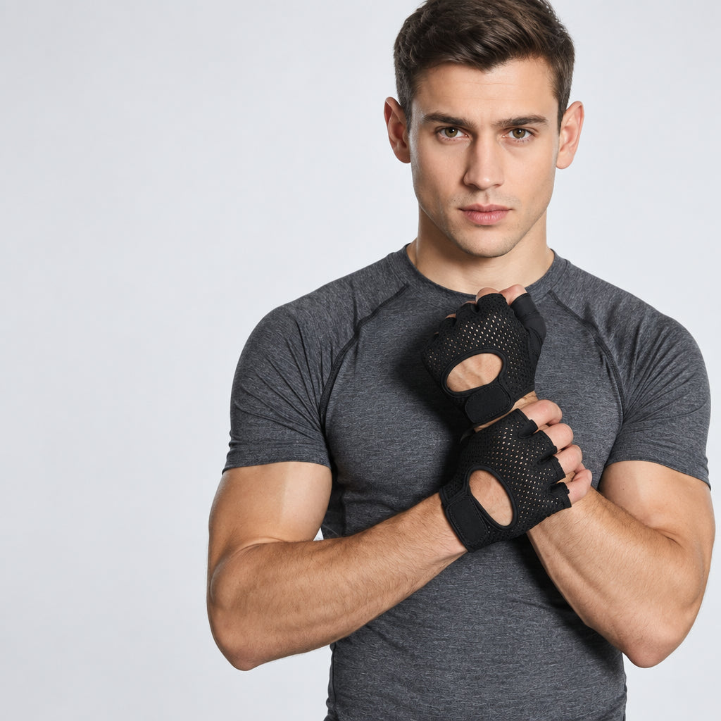 A man in a grey athletic t-shirt wearing black fingerless grip strengthener weightlifting gloves with green logo details, posing in front of a chain-link fence in a gym setting.