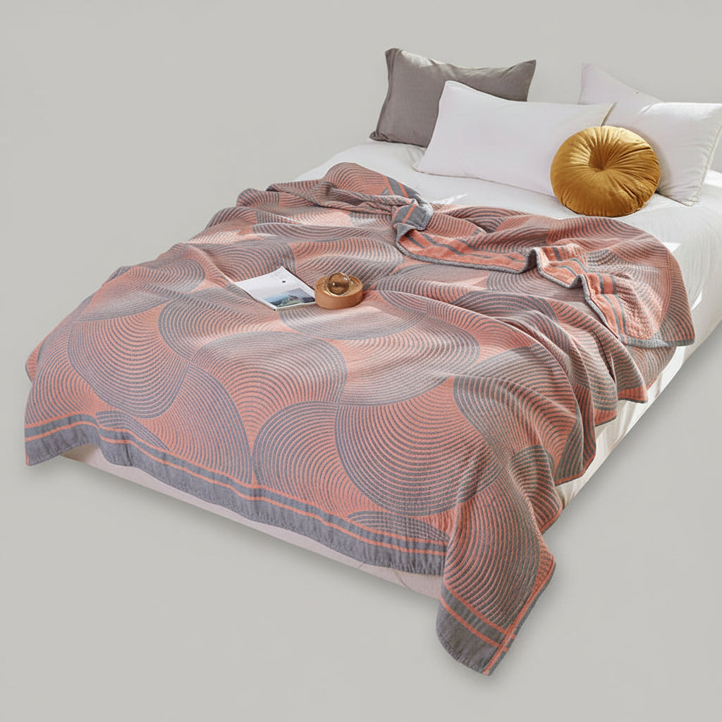 Patterned throw blanket on a bed with pillows and a window in the background